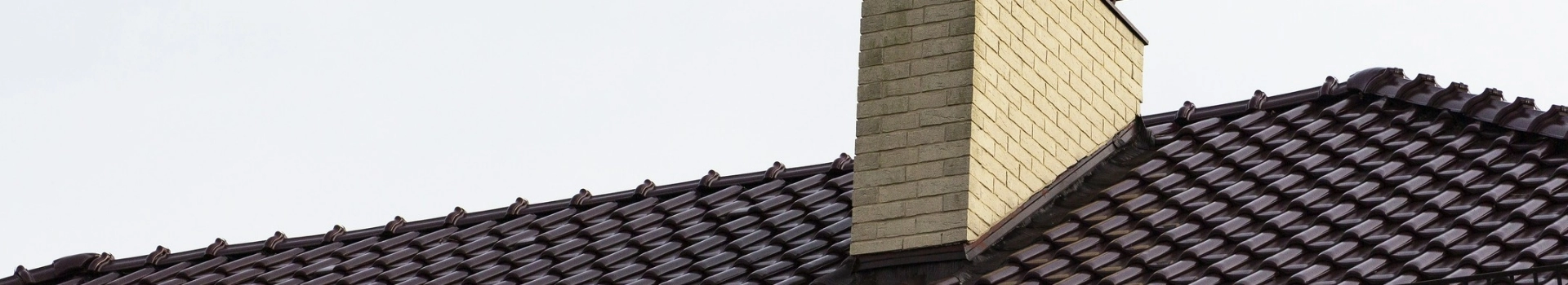Komin z jasnej cegły na ciemnym dachu